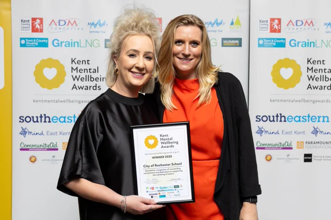 Two people are stood smiling and one is holding the award winner's certificate.
