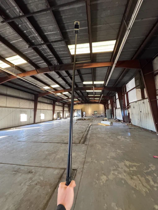 PermitZIP Engineer holds an extended pole with an Insta360 camera inside a large, empty warehouse during a site survey.