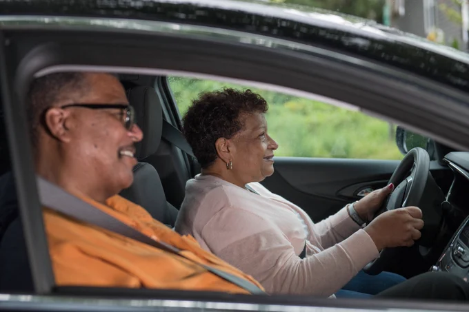 Older couple in a car, with a woman driving.