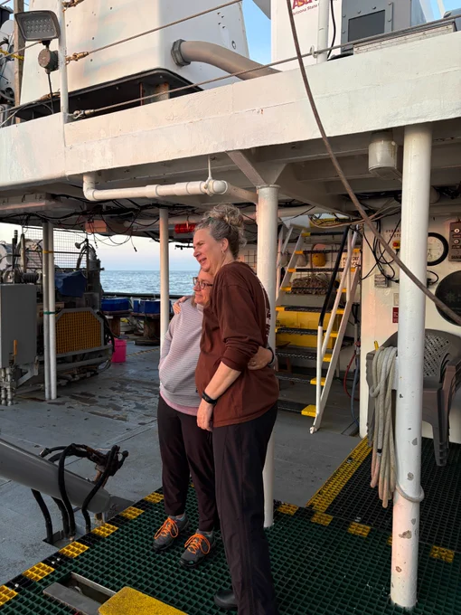 Co-chief scientists Elizabeth Kujawinski and Sonya Dyhrman hug and reflect as they watch the sunrise from the deck of the R/V Atlantic Explorer at the end of the second C-CoMP cruise, AE2520. Photo by Erin Maybach. 