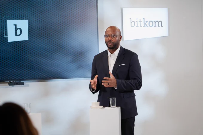Das Bild zeigt Armand Zorn, den stellvertretenden Fraktionsvorsitzenden der SPD-Bundestagsfraktion , beim Bitkom@eight. Er steht an einem weißen Stehpult in einem hell ausgeleuchteten Studio. Er trägt einen dunkelblauen Anzug mit weißem Hemd, Einstecktuch und Brille. Seine Hände sind vor dem Körper gehoben und unterstreichen gestisch seine Aussagen. Vor ihm stehen ein Glas Wasser und eine weiße Tasse mit Untertasse sowie ein Smartphone.  