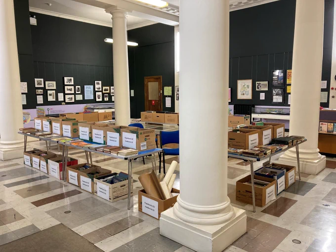 Boxes of books on tables in the middle of a library exhibition space.