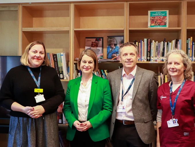 Helen Hayes MP standing and smiling with Steve Smith, CEO of St Christopher's, and other members of the St Christopher's team. The four are stood in front of a wall of bookshelves.