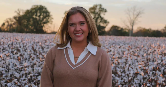 Person smiling in a cotton field at sunset.