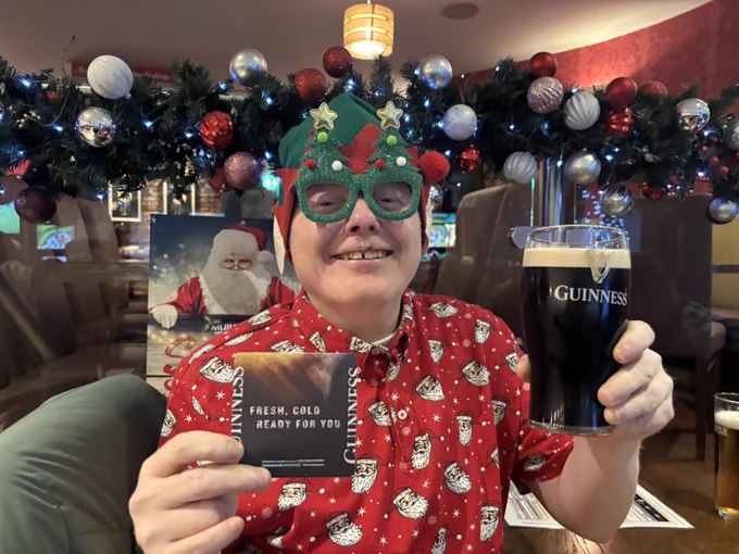 Kevin wearing his Father Christmas shirt, Elf hat and Christmas Tree glasses, holding a pint of Guinness, Cheers.