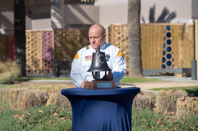 Person in a white uniform ringing a bell at a ceremonial event outdoors.