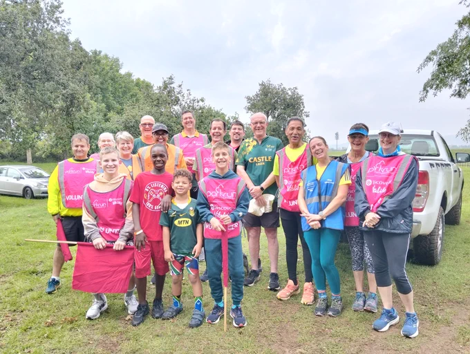 A group of parkrun volunteers smiling and standing outdoors with trees in the background.