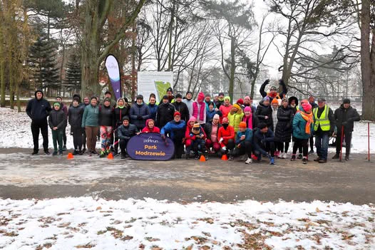 A group of parkrunners and volunteers smiling for a photo in a snowy park in Modrzewie.  