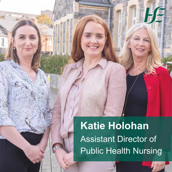 Three women, dressed in formal clothes stand smiling, in front of a building. The text reads, "Katie Holohan, Assistant Director of Public Health Nursing."