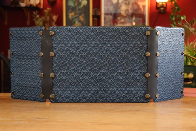 A blue leather DM screen made of three panels, standing upright on a table