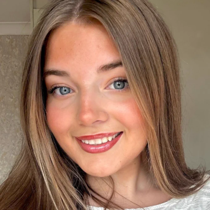 A photograph of article author, Libby Brown. Libby is wearing a white patterned top, her long brown hair is down and she's smiling at the camera.