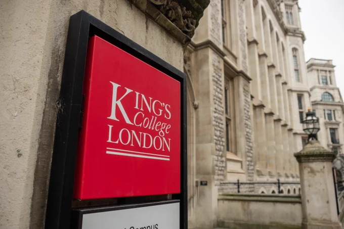 Red sign with white text reading King's College London mounted on a stone building exterior in an urban setting.