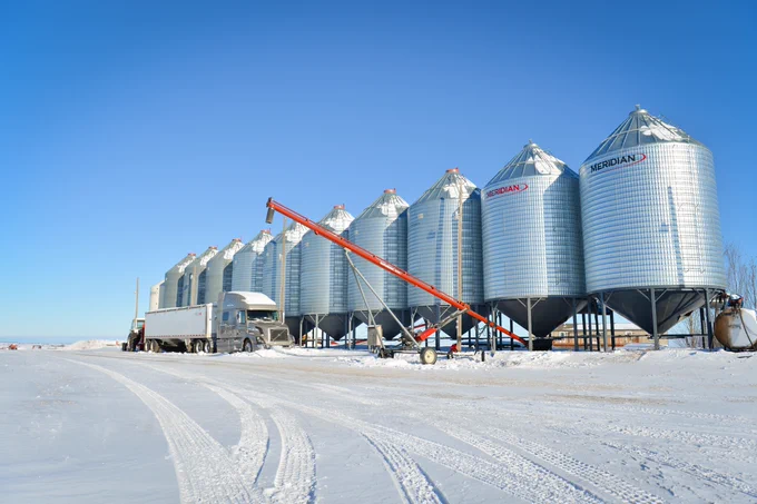 Grain bins lined up in the winter with a blue sky.  