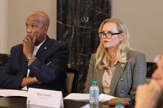 A man in a navy jacket and a woman in a plaid jacket look at a presentation during a meeting