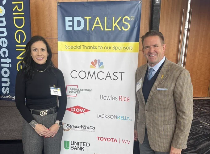 teacher standing next to a sign with another man both planning on presenting at a conference 