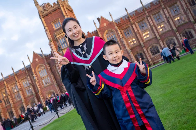 Image shows a graduate and her five-year-old son pictured in front of the Lanyon Building. They are both doing the peace symbol with their hands.