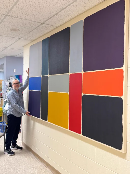 Dr Michael Weinberg of ArtWorks for Cancer poses with a vibrant work by Barbara Caruso entitled Colour Lock, Black and Grey Series #14 freshly installed in a hallway at Orillia Soldiers' Memorial Hospital (OSMH).