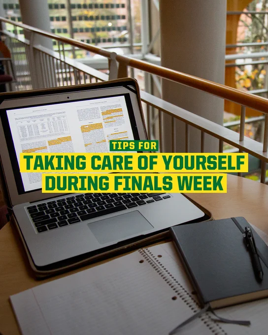 Laptop open on a webpage titled "Tips for Taking Care of Yourself During Finals Week," with a notebook and pen beside it, situated on a wooden table near a railing with a view of trees and a building through the window.