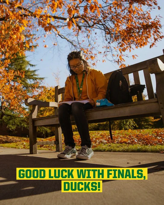 Student studies on a bench under autumn trees at the University of Oregon, with a message saying 'Good luck with finals, Ducks!'