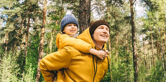 Two people in matching yellow jackets enjoying a piggyback ride in a lush forest