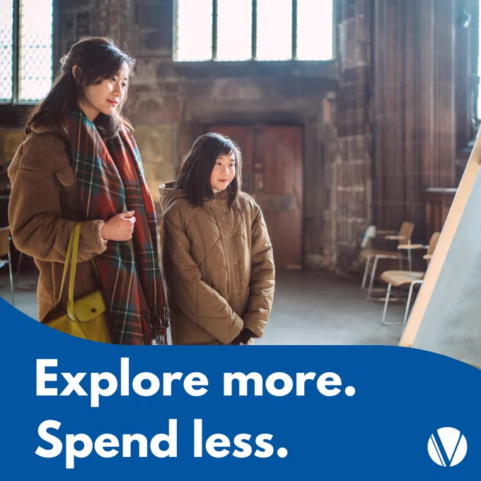 A mother and daughter in winter coats, examining an exhibit beside a window, with a text overlay that reads 'Explore more. Spend less.'