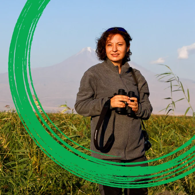 A woman holding binoculars stands in Armenia's Armash wetlands