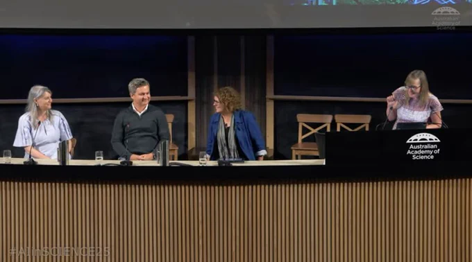 Three people sit at a bench. Another stands at a lectern. The logo of the Australian Academy of Science is on the lectern. 