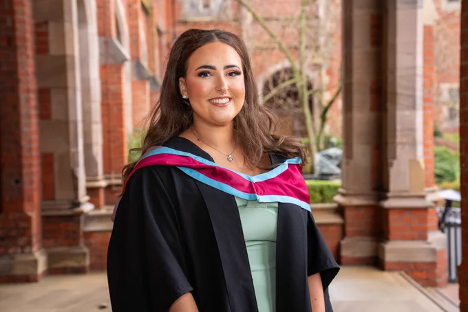 Image shows Tanisha Wallace pictured in the Cloisters at Queen's. She is wearing her graduation gown.