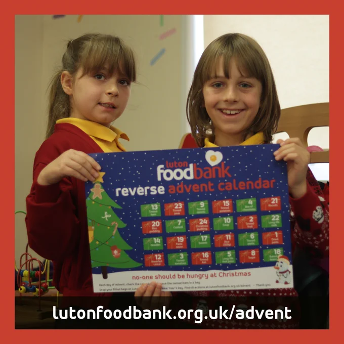 Two smiling school children show their Luton Foodbank Reverse Advent Calendar. lutonfoodbank.org.uk./advent