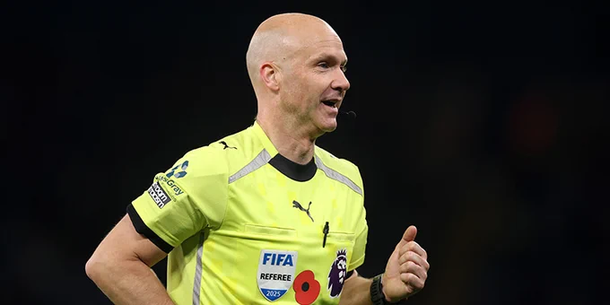 A FIFA referee wearing a bright yellow uniform with a logo, jogging on a soccer field during a night game.