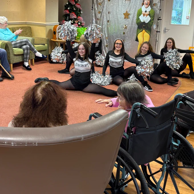 Four Laurus Ryecroft Students performing their cheerleading routine for residents of Daisy Nook House Care home, who are all clapping in a circle around them.