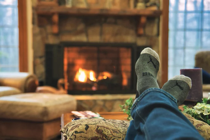 A fireplace with a glowing fire going, shown from the POV of a person lounging on a couch across the room. They're wearing cozy knit socks.