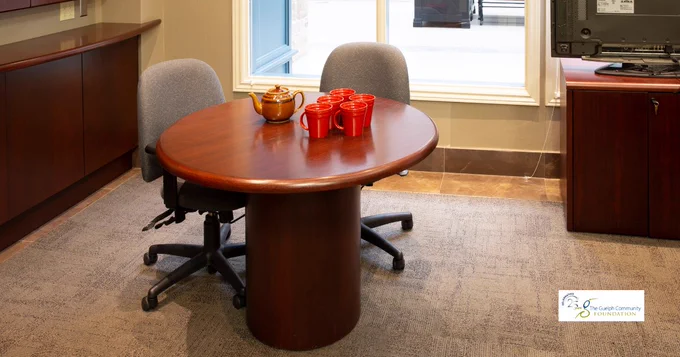 Boardroom with a small table with two chairs, a brown tea pot, four orange mugs, and a window at The Guelph Community Foundation office