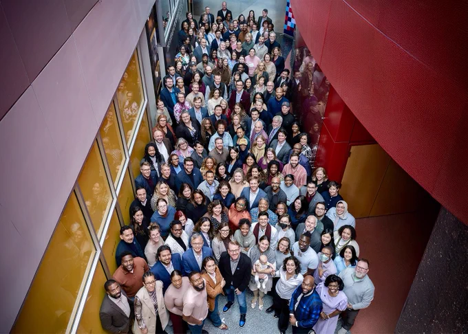 A large group of people gathered in an indoor space with colorful walls, looking up towards the camera, representing a diverse workforce.