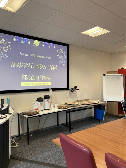 Conference room set up with a projector screen displaying 'Academic New Year Resolutions' and tables with refreshments and coffee.
