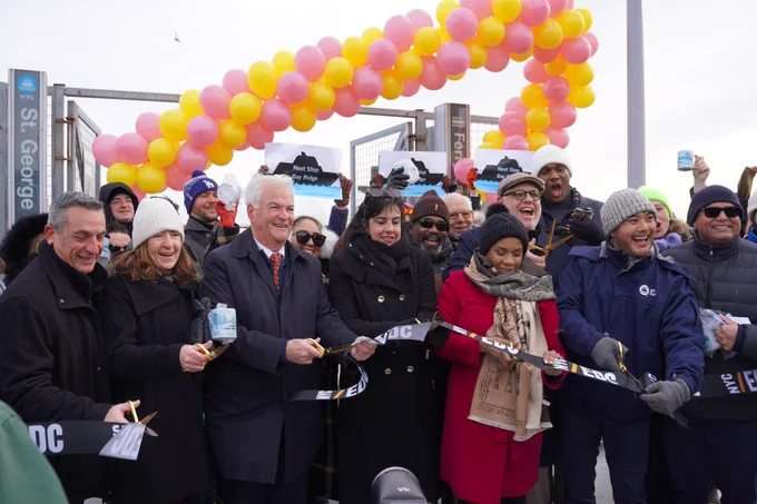 Deputy Public Advocate Hussain, elected officials and community leaders smile as they cut an EDC ribbon in front of a ferry dock entrance for the St. George route, flanked by a banner of pink and yellow balloons