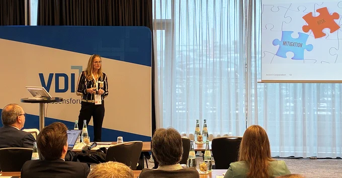 Speaker presenting at a trade conference with a puzzle piece logo displayed on the right