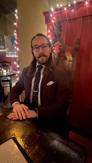 Me sitting in a throne-like chair at The Publick House in Brookline. Burgundy suit, navy tie with white dots. I'm posing proudly, with humorously regal stiffness.