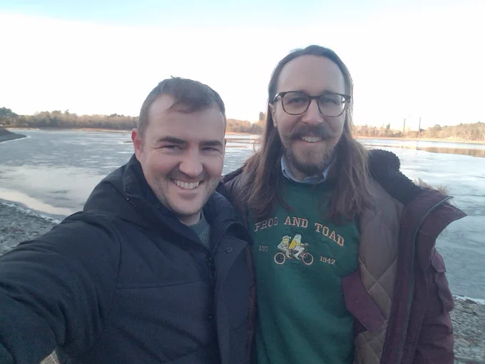 My best friend Max takes a selfie of him and me walking along the Chestnut Hill Reservoir. Behind us, the reservoir has begun to ice over, and the distant trees are nearly bare. The sky looks clear. We're in winter coats: Max's is black, mine is burgundy. You can also see my green embroidered Frog and Toad sweatshirt, a dissertation-defense gift from Max and Ashley. We're smiling.