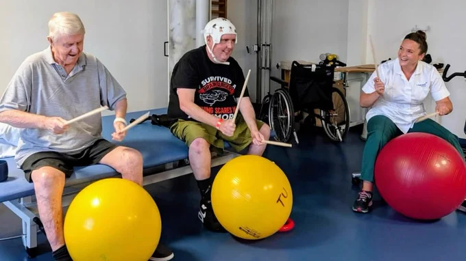 2 male patients and 1 woman with drumsticks and large inflatable exercise balls
