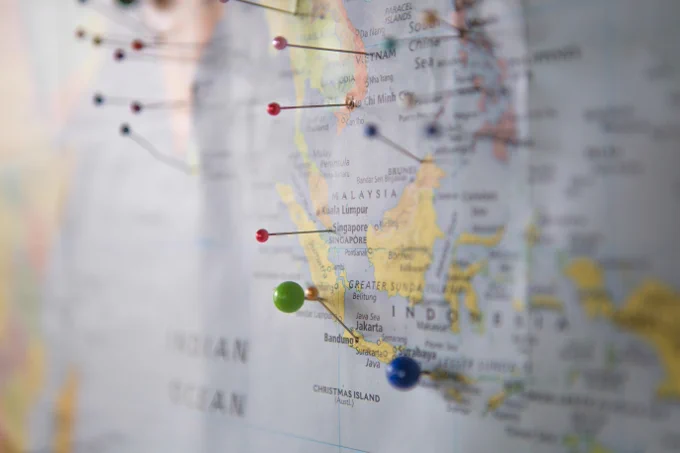A photograph of a world map marked with colored pins at various locations of Southeast Asia, with a close-up focusing on Indonesia. By "Z" under a free Unsplash license: https://bit.ly/4qgUjgJ.