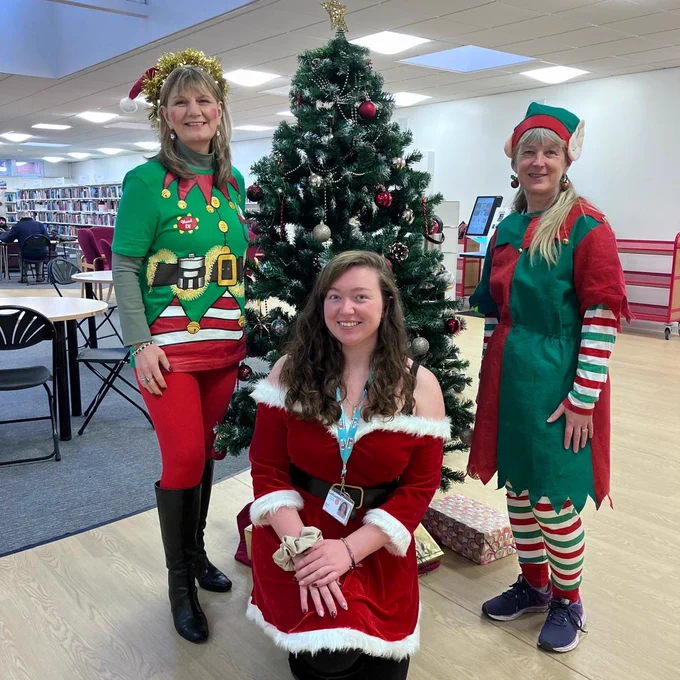 Three staff members, two elves and Santa, stood in front of a Christmas tree at Chorley library