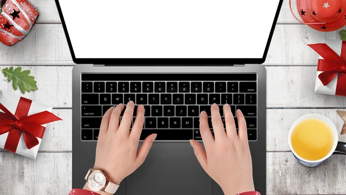 Hands typing on a keyboard surrounded by festive decorations. 