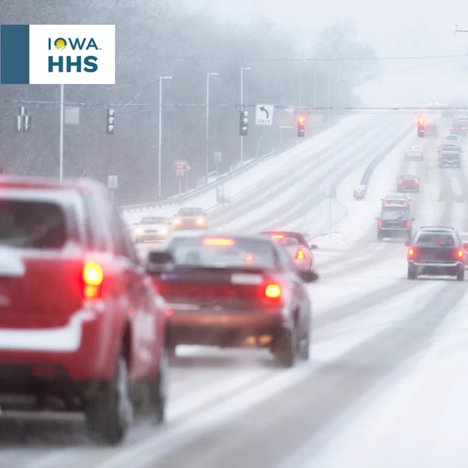 Vehicles driving on a snowy road with visible traffic lights and an Iowa HHS sign.
