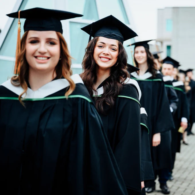 A group of university graduates in black caps and gowns smiling as they walk at a graduation ceremony.