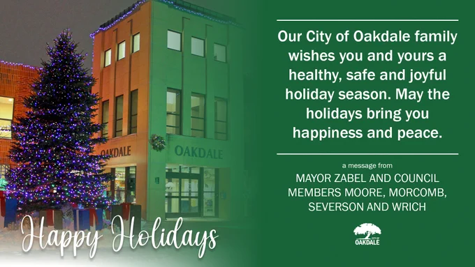 graphic with image of a large pine tree with lights to left and front of a building illuminated at night that reads "OAKDALE" on the side and front of the brown entry tower with white text at the bottom in script that reads "Happy Holidays" with green section on the other half that reads in white text "Our City of Oakdale family wishes you and yours a healthy, safe and joyful holiday. May the holidays bring you happiness and peace. a message from MAYOR ZABEL AN COUNCIL MEMBERS MOORE, MORCOMB, SEVERSON AND WRICH" with a white logo below of a tree that reads "CITY OF OAKDALE"