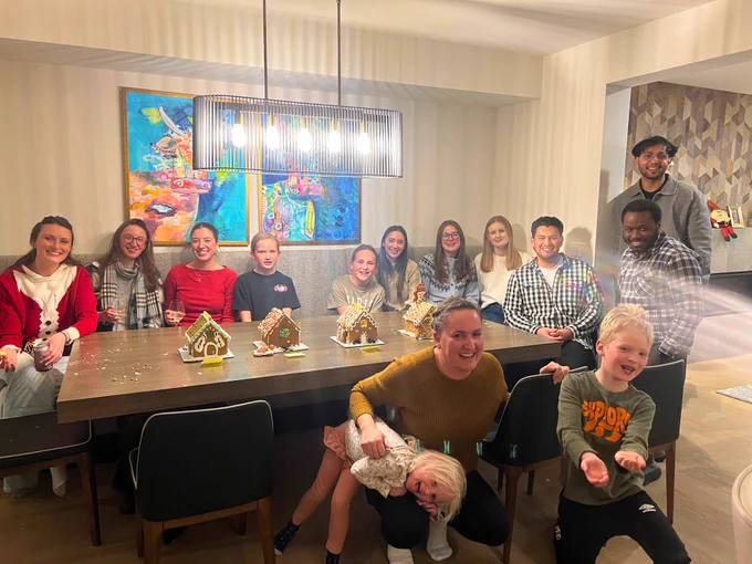 A Holiday photo of the ENHANCE Lab team and family sitting around a table with 4 gingerbread houses.