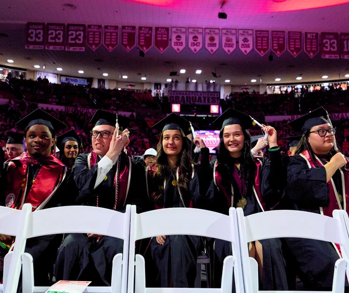 Graduates wearing caps and gowns smiling and waving during a commencement ceremony at OU.