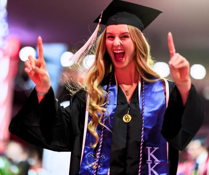 Graduating student in a cap and gown joyfully flashing a victory sign at a graduation ceremony.