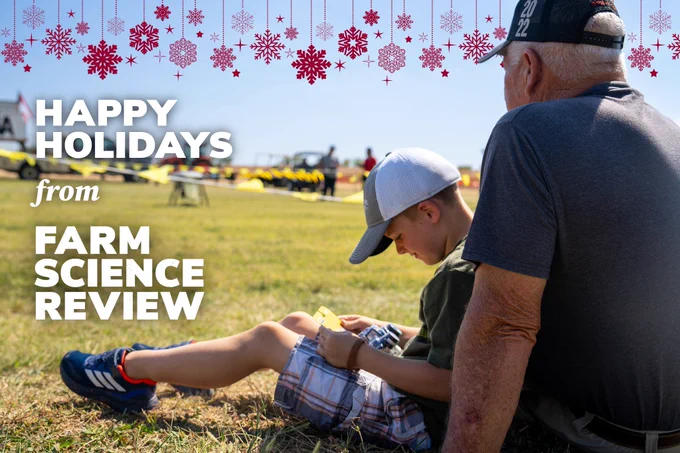 A boy and his family member sitting in a field during a demonstration at Farm Science Review. There is a red snowflake design at the top of the image and text that reads, "Happy Holidays from Farm Science Review."